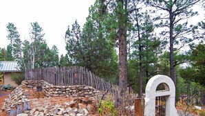 A rustic stone wall, a wooden fence, and a white arched gate in a wooded area. - Quiet Ruidoso Hideaway - 2 Mi to Grindstone Lake! (Ruidoso)