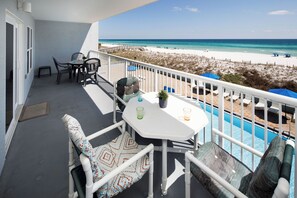 A balcony with a table and chairs, a pool, and a beach view.