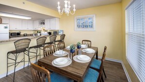 A dining area with a wooden table set for six, surrounded by wicker chairs with blue cushions. - IBR 3006: Sandy Smiles - Unbeatable Location, Unmatched Oceanfront Views! (Fort Walton Beach)