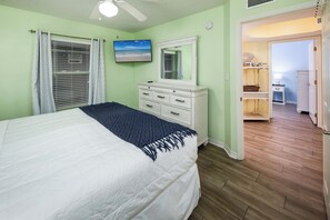 Quarto com cama, cómoda, televisão e porta que dá para outro espaço.