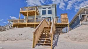 Una casa frente a la playa de dos pisos, con una escalera de madera que lleva a un balcón.