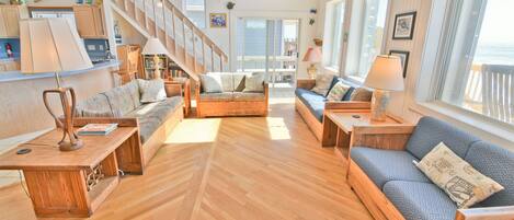 A spacious living area with wooden flooring, a staircase, and large windows offering a view of the sea.