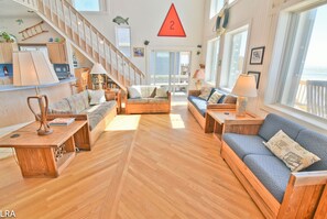 Amplia sala de estar con piso de madera, una escalera y ventanas grandes con vista al mar.