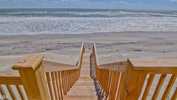 Una escalera de madera que lleva a una playa con vista despejada al océano.