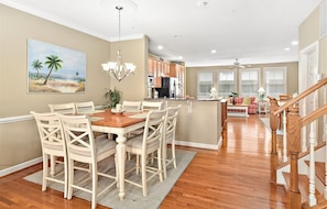 A spacious dining area with a wooden table and white chairs, a kitchen with wooden cabinets, and a staircase leading to another level.