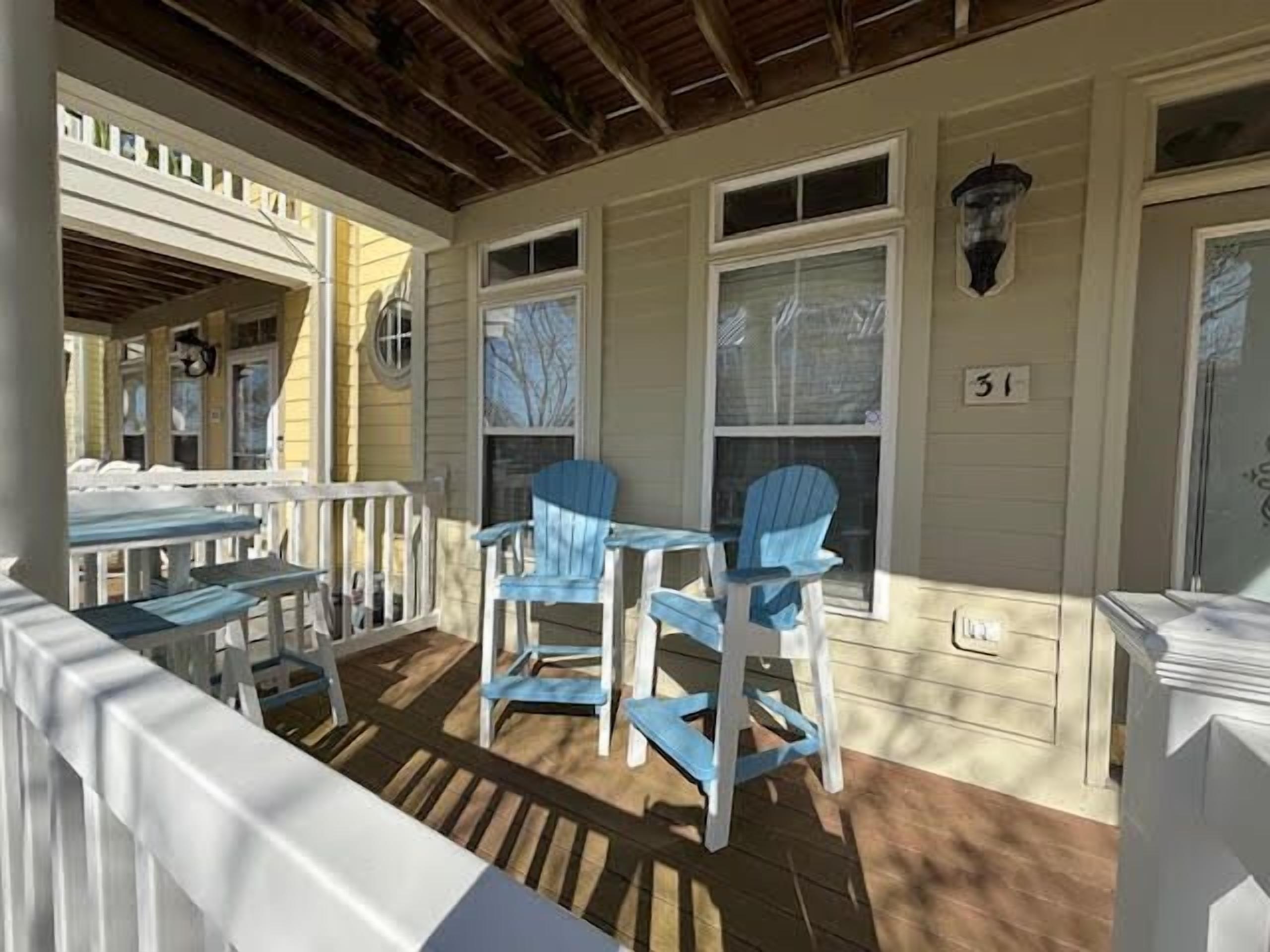 A covered porch with a wooden floor, white railings, and blue Adirondack chairs.