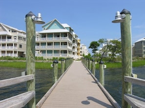 A wooden boardwalk leading to a waterfront property with multiple balconies and a green roof.