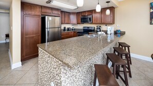 Eine Küche mit Granit-Arbeitsplatten, Holzschränken und Edelstahlgeräten, sowie einer Bar mit Hockern.