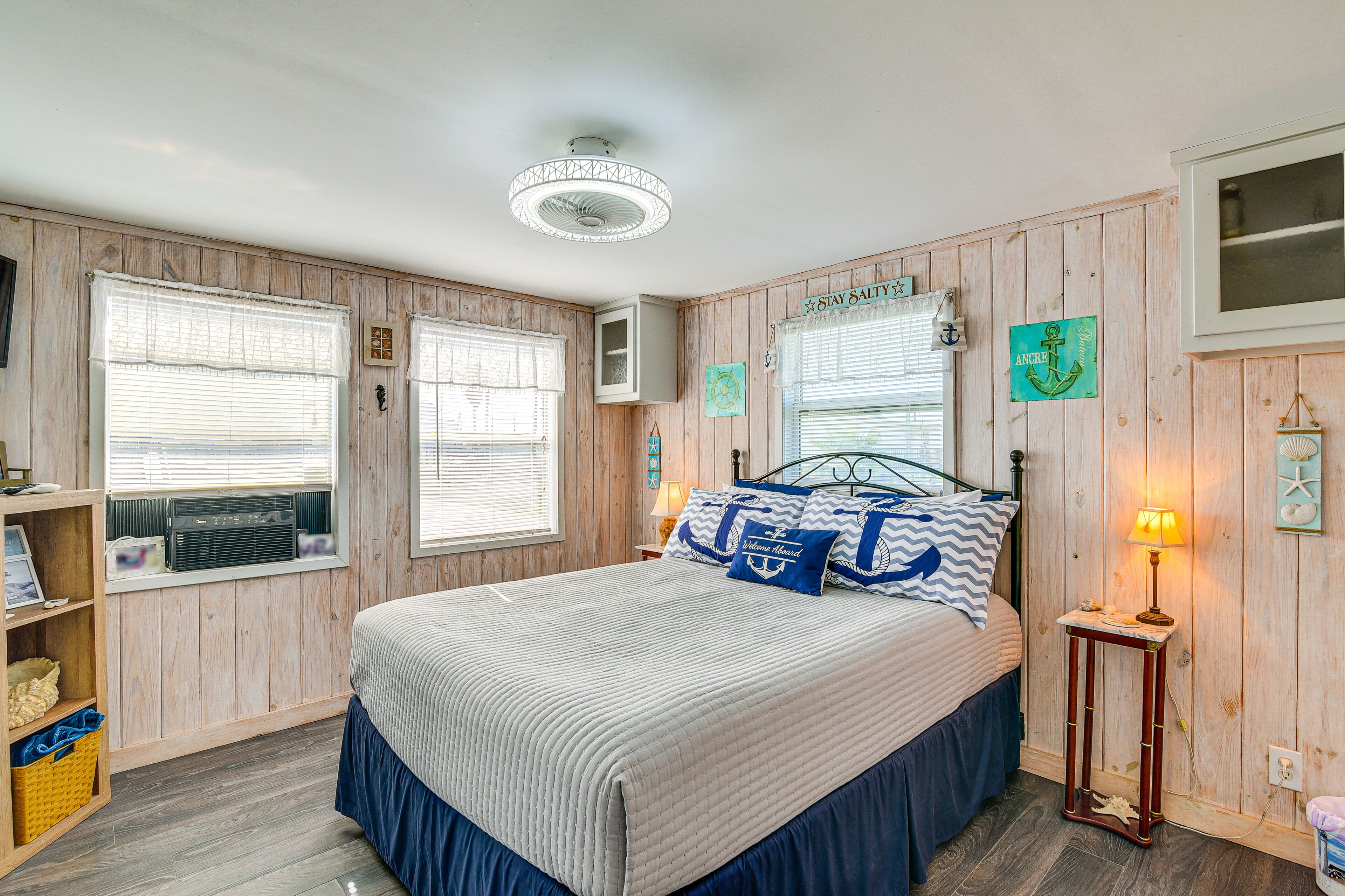 A bedroom with a bed, wooden walls, a ceiling fan, and a window with blinds.