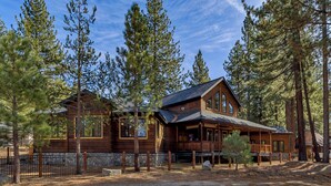 A large wooden cabin with multiple windows and a porch, surrounded by tall pine trees.