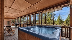 A wooden deck with a hot tub, outdoor seating, and a view of trees.