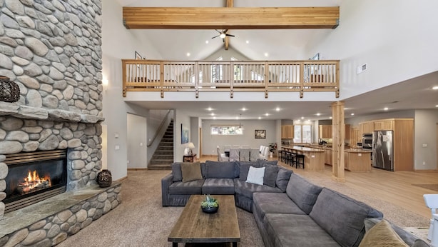 A spacious living area with a stone fireplace, a large sectional sofa, a wooden coffee table, and a kitchen in the background.