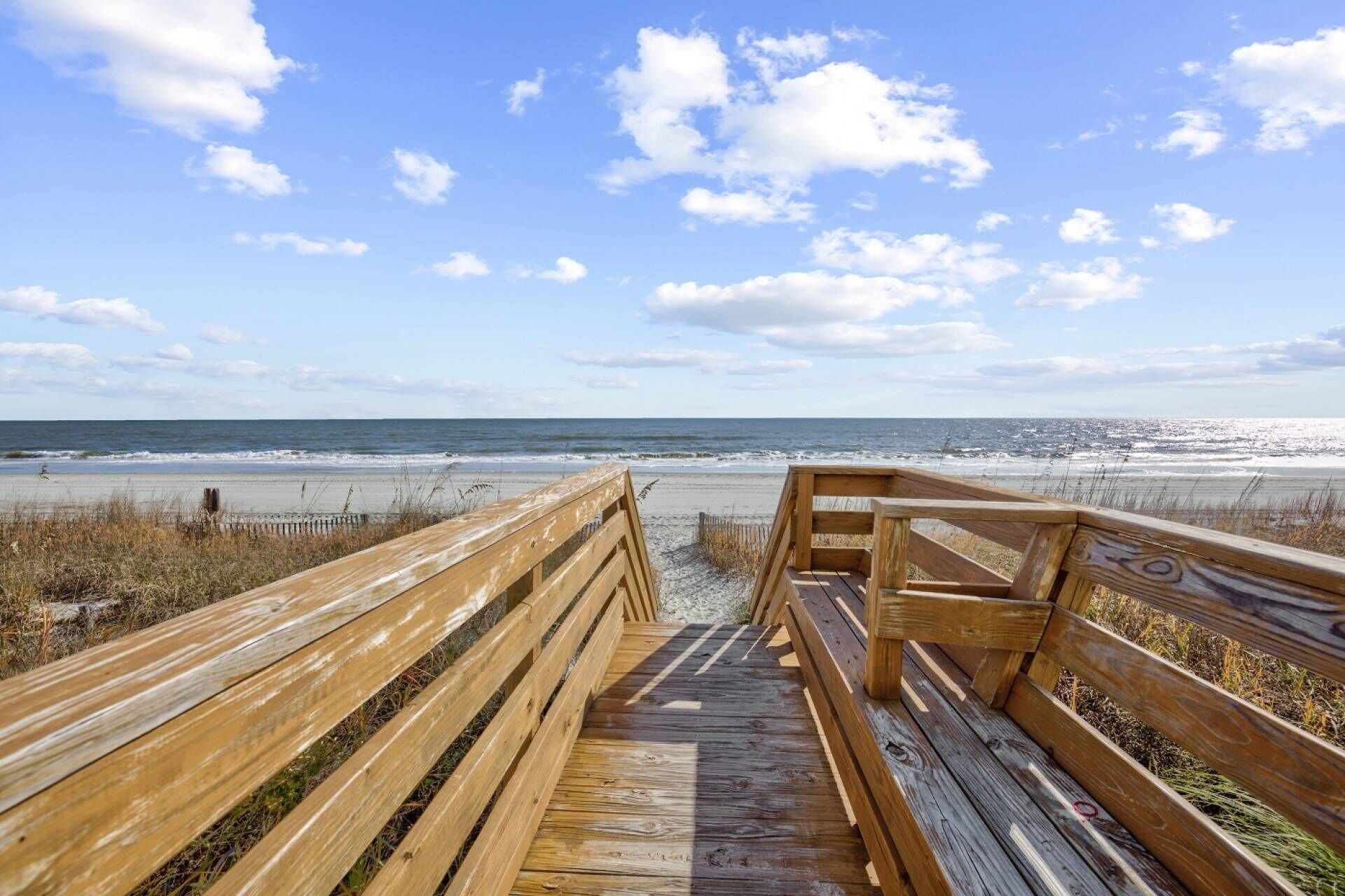A wooden boardwalk leading to a beach with a clear view of the ocean.