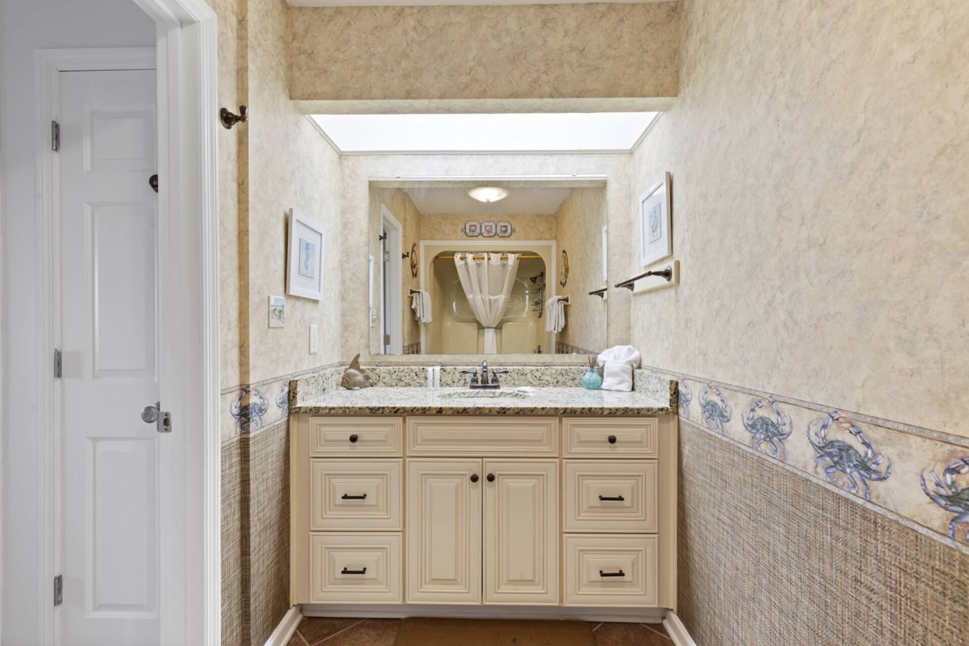A bathroom with a large mirror, a sink with a granite countertop, and a vanity with multiple drawers.
