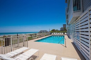 A rooftop pool with a view of the ocean, white lounge chairs, and a lifeguard sign.