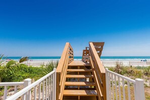A wooden boardwalk leading to a beach with white railings.