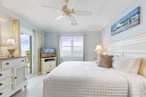 Quarto com cama grande, ventilador de teto, televisão e janela com vista para o oceano.