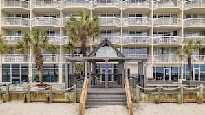 A beachfront hotel with multiple balconies, a central entrance with a sign, and a sandy beach area. - *Fall into Savings-20% Off New Bookings thru 2026* (Murrells Inlet)