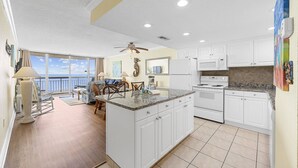 A spacious kitchen with white cabinets, a granite countertop, and a large island. There is a dining area with a table and chairs, and a balcony with a view of the ocean. - *Fall into Savings-20% Off New Bookings thru 2026* (Murrells Inlet)