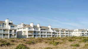 Une rangée d’immeubles résidentiels à plusieurs étages, dotés de balcons, située sur une colline verdoyante sous un ciel dégagé.