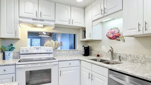 A kitchen with white cabinets, a stove, a sink, and a coffee maker.