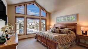 Une chambre à coucher avec un grand lit, une table de chevet, une commode et une fenêtre donnant sur un paysage enneigé.