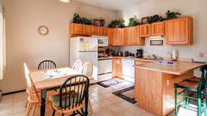 A kitchen with wooden cabinets, a refrigerator, microwave, and a sink. There is a clock on the wall and a sign that says "Apples".