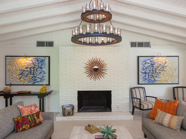 A spacious living room with a fireplace, two sofas, a coffee table, and a chandelier. - Hidden Haven - Spanish Revival Pool Retreat (Palm Springs)