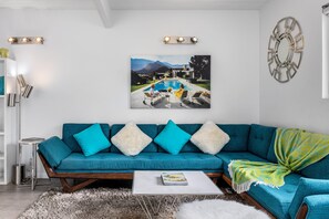 A living room with a teal sofa, a coffee table, and a painting of a pool and mountains.