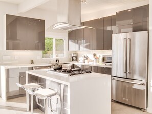 A modern kitchen with stainless steel appliances, a central island with bar stools, and large windows.