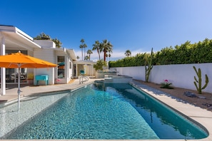 A modern pool area with a clear pool, a blue umbrella, and a white building with a patio.