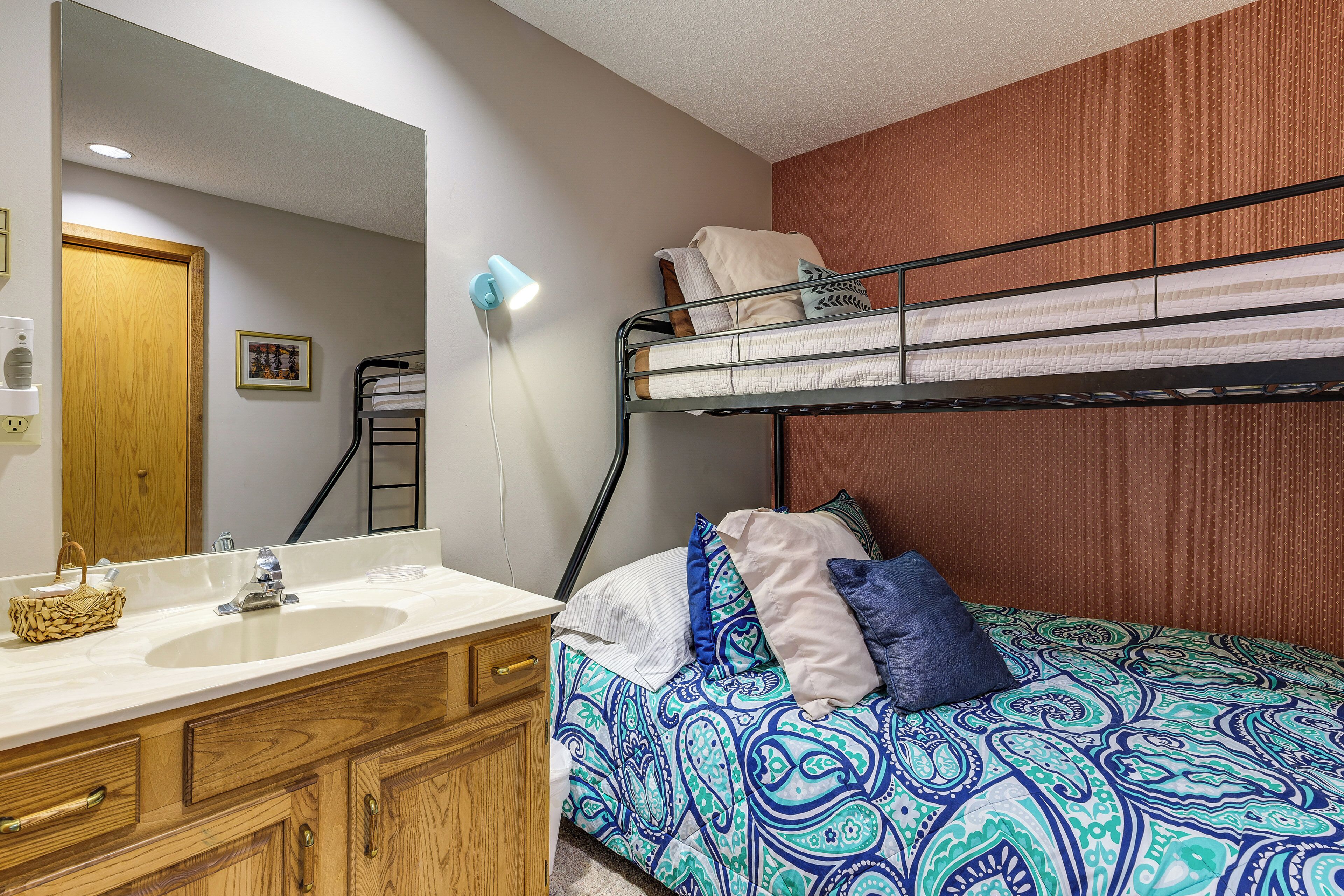 A bunk bed with a patterned bedspread, a wooden vanity with a sink, and a mirror.
