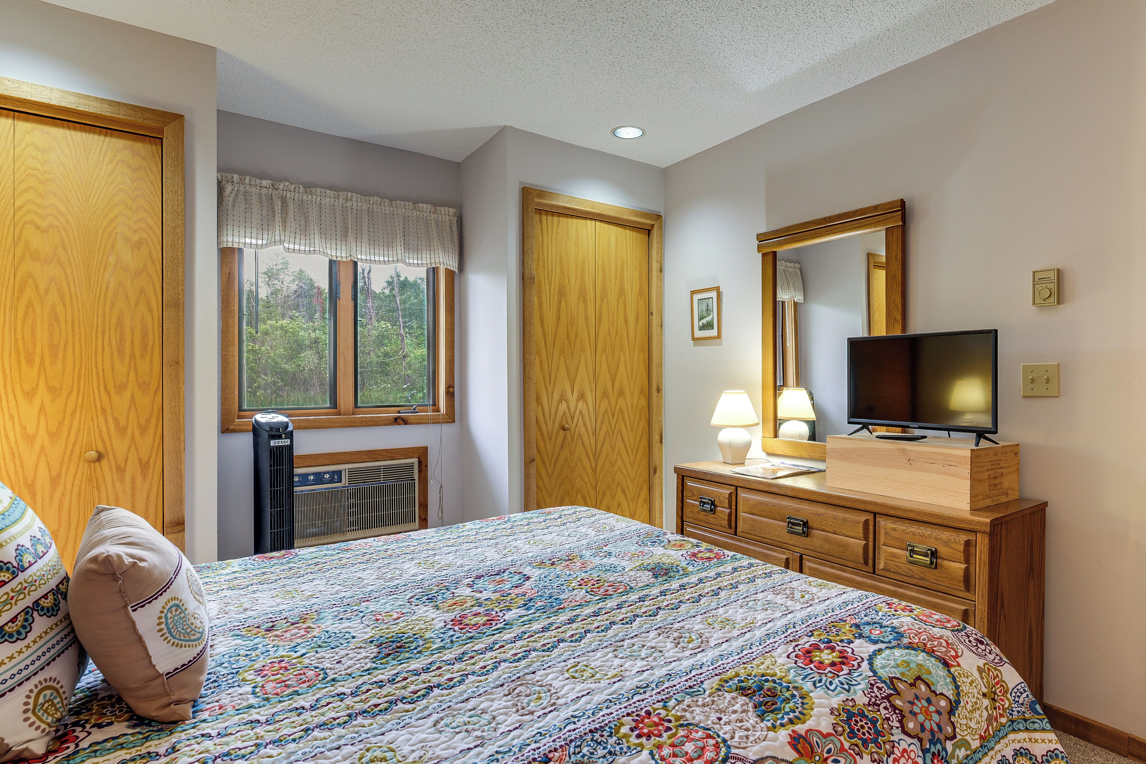 A bedroom with a bed, a television on a dresser, a window with curtains, and a radiator.