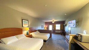 Une chambre d’hôtel avec deux lits, un bureau, une chaise, un ventilateur de plafond et une fenêtre avec des rideaux.