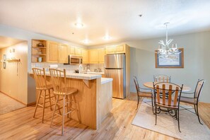 A modern kitchen with wooden cabinets, a stainless steel refrigerator, and a bar area with stools.