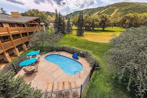 A pool area with a wooden deck, lounge chairs, and umbrellas.