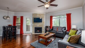 Una sala de estar con chimenea, ventilador de techo, televisor y comedor con mesa y sillas.