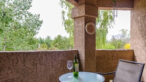 Una mesa de vidrio con una botella y una copa de vino en un balcón que ofrece vistas a árboles.