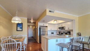 A modern kitchen with white cabinets, stainless steel appliances, and a central island with bar stools. - Dirft into Surf Condos 414 - Dolphins Drift! (Surf City)