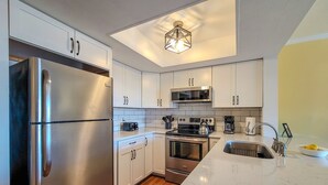 A modern kitchen with stainless steel appliances, white cabinets, and a skylight. - Dirft into Surf Condos 414 - Dolphins Drift! (Surf City)