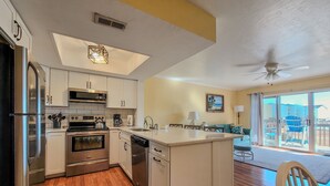 A modern kitchen with white cabinets, stainless steel appliances, and a wooden floor. - Dirft into Surf Condos 414 - Dolphins Drift! (Surf City)