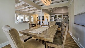 Un vaste espace dédié à la salle à manger, avec une table et des chaises en bois, un centre de table décoratif représentant un voilier, et une cuisine moderne en arrière-plan.