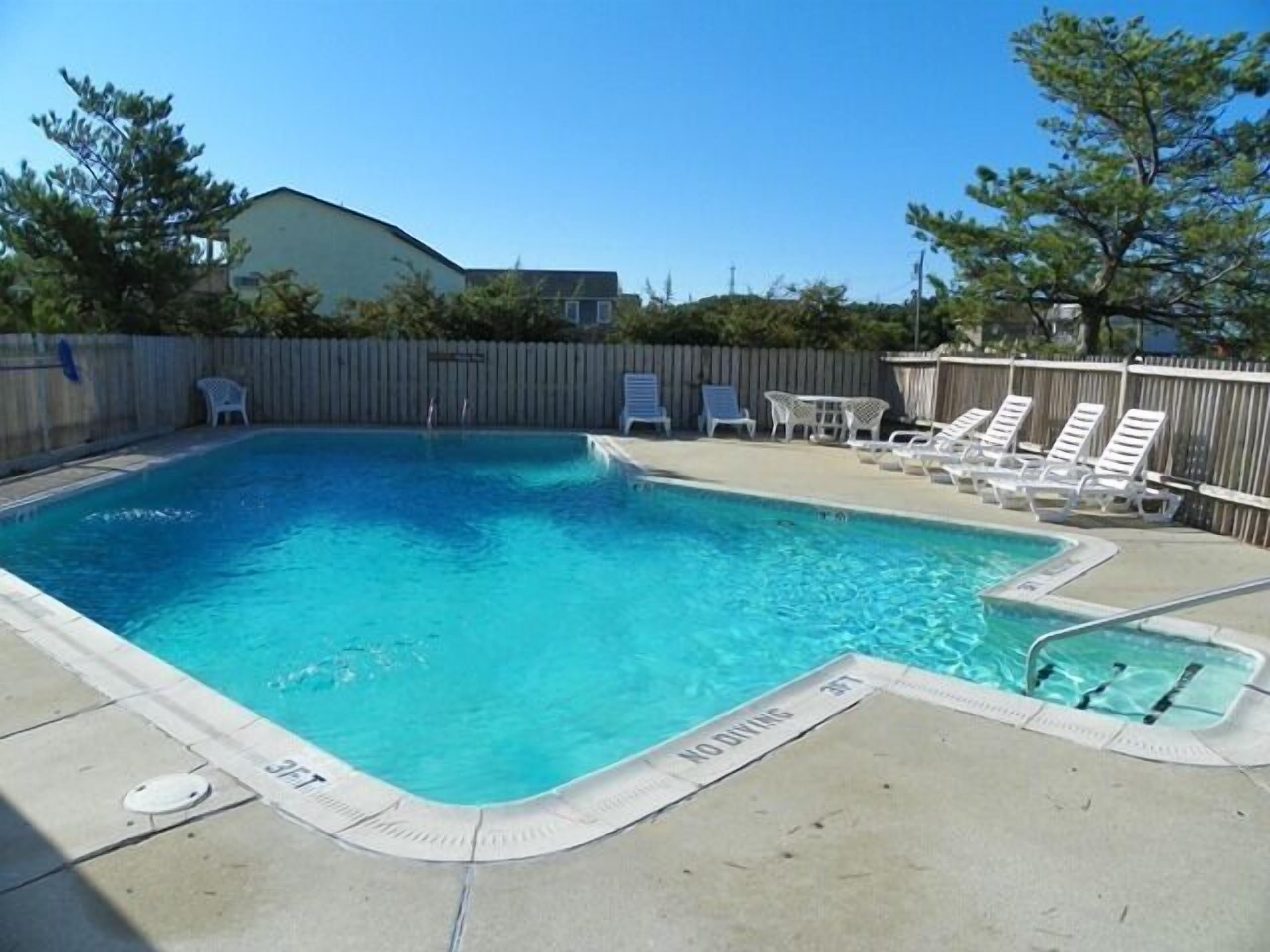 Una piscina rectangular con un letrero que dice 'NO DIVING', rodeada de sillas de descanso y una valla de madera.