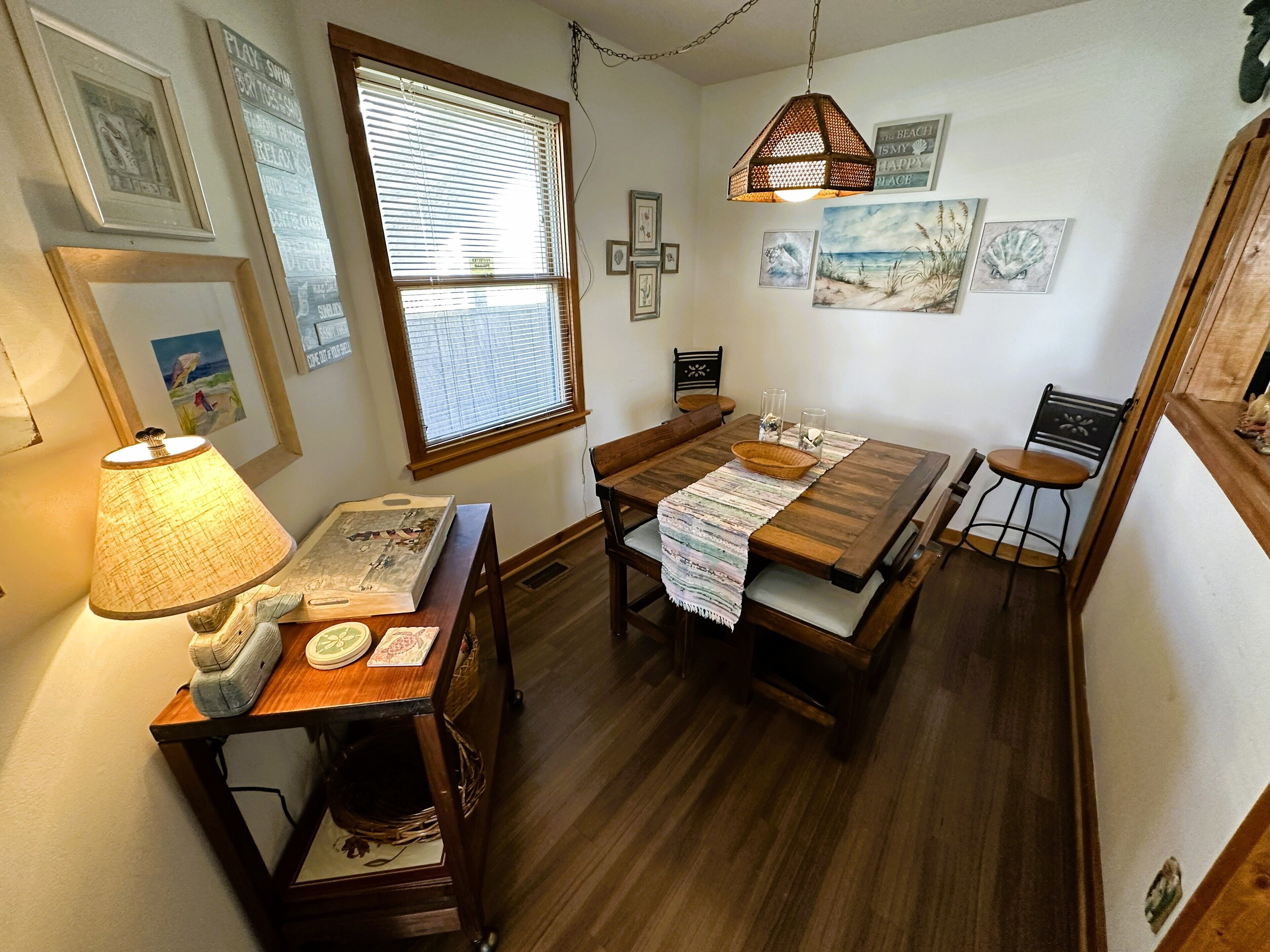 A dining area with a wooden table, chairs, a lamp, and artwork on the walls.