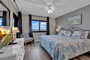 Une chambre à coucher comprenant un lit, un bureau, une chaise, un ventilateur de plafond, une fenêtre avec vue et un tableau.