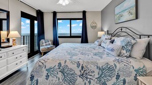Une chambre avec un grand lit, un ventilateur de plafond, une commode, une chaise et une vue sur l’océan.