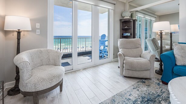 A living room with a view of the ocean, a sliding glass door, a blue chair, a beige armchair, and a blue sofa. - Inn at Crystal Beach 408 * Gulf Front with Beach Chair Set. Onsite dining! (Destin)
