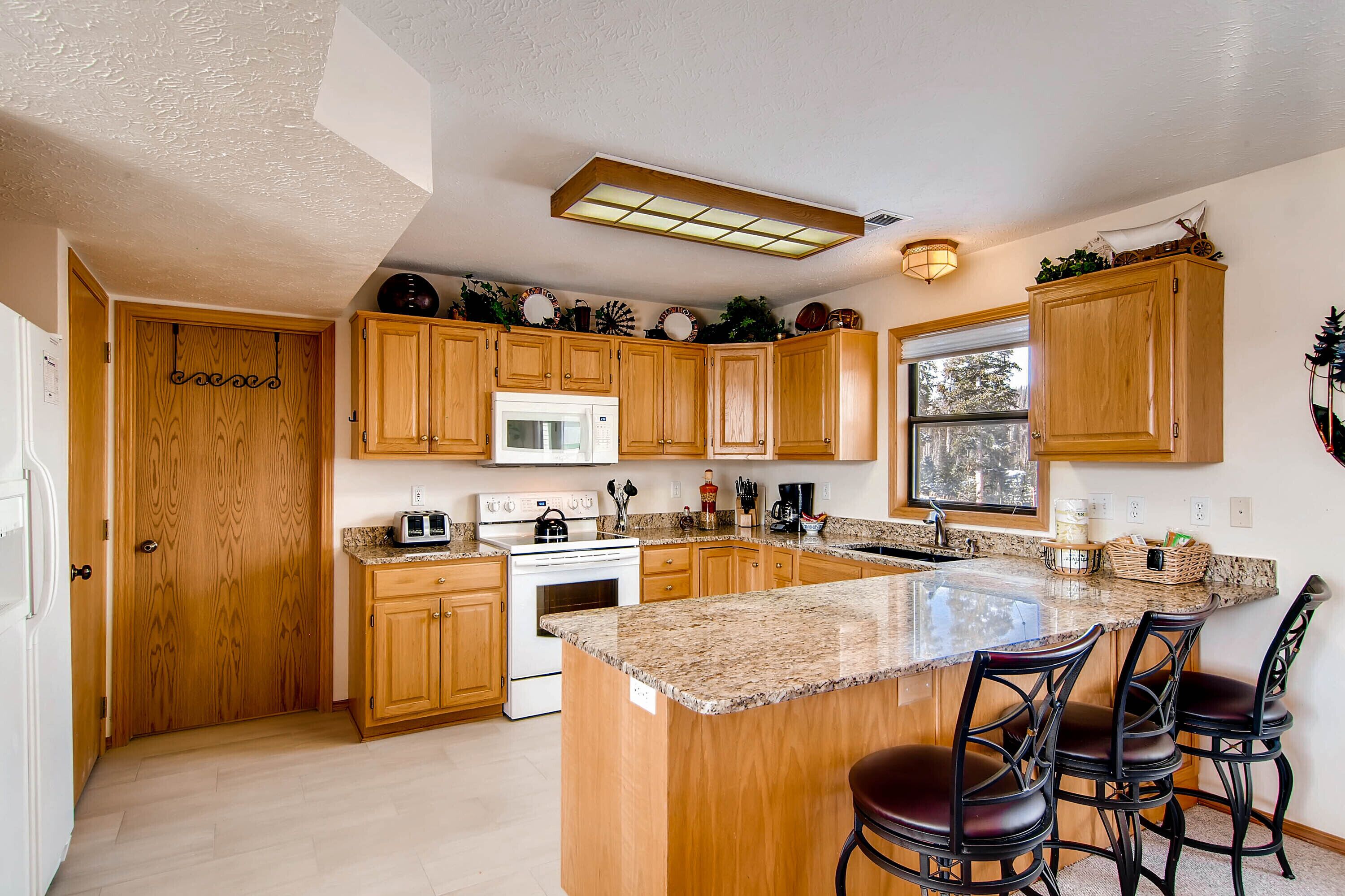 A kitchen with wooden cabinets, a granite countertop, a built-in oven, and a large island with bar stools.