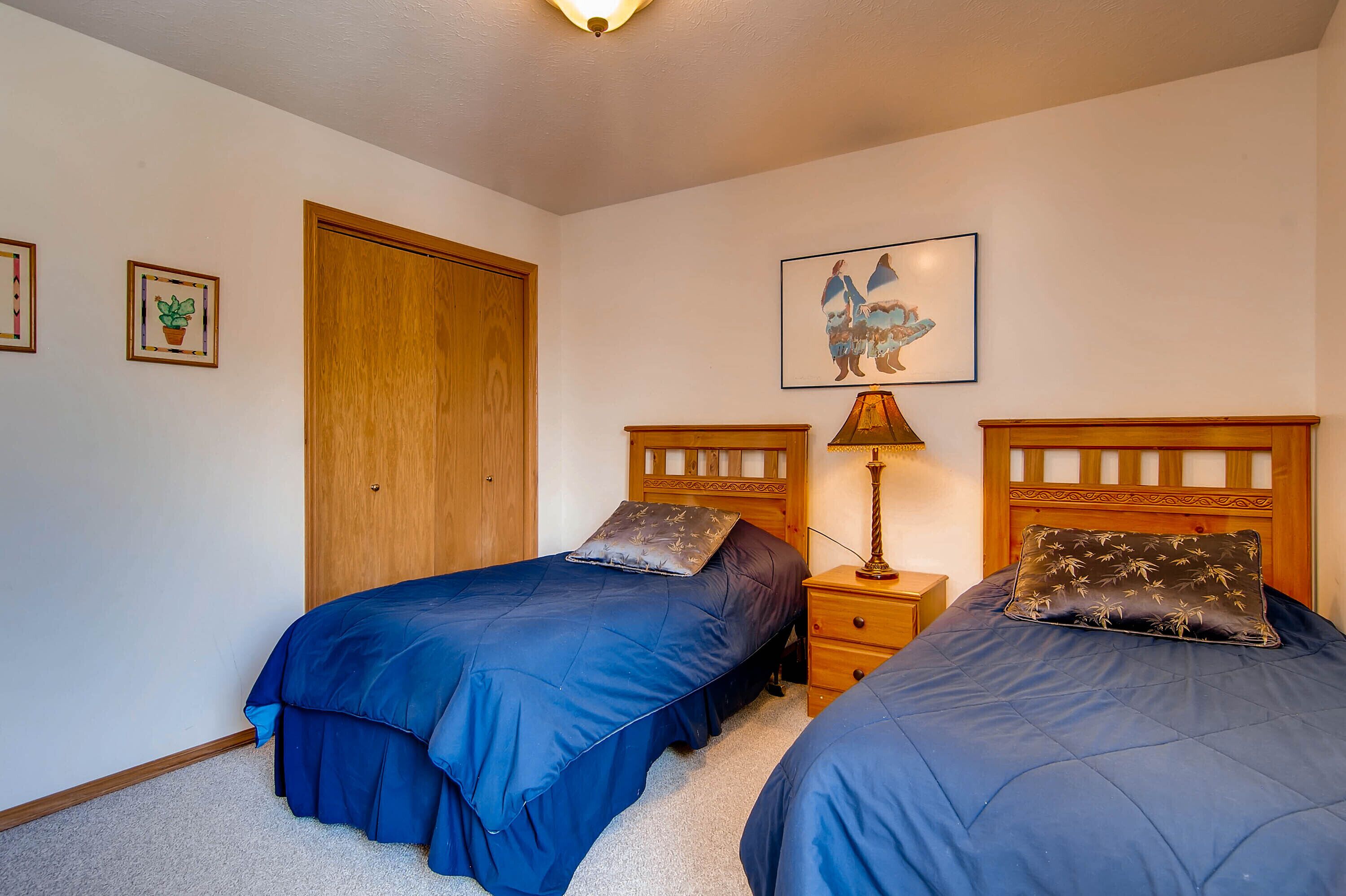A bedroom with two beds, a wooden wardrobe, a nightstand, and a wall-mounted lamp.