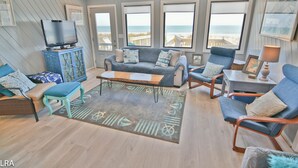 Amplia sala de estar con un ventanal con vista a la playa, un televisor sobre un mueble y asientos cómodos.